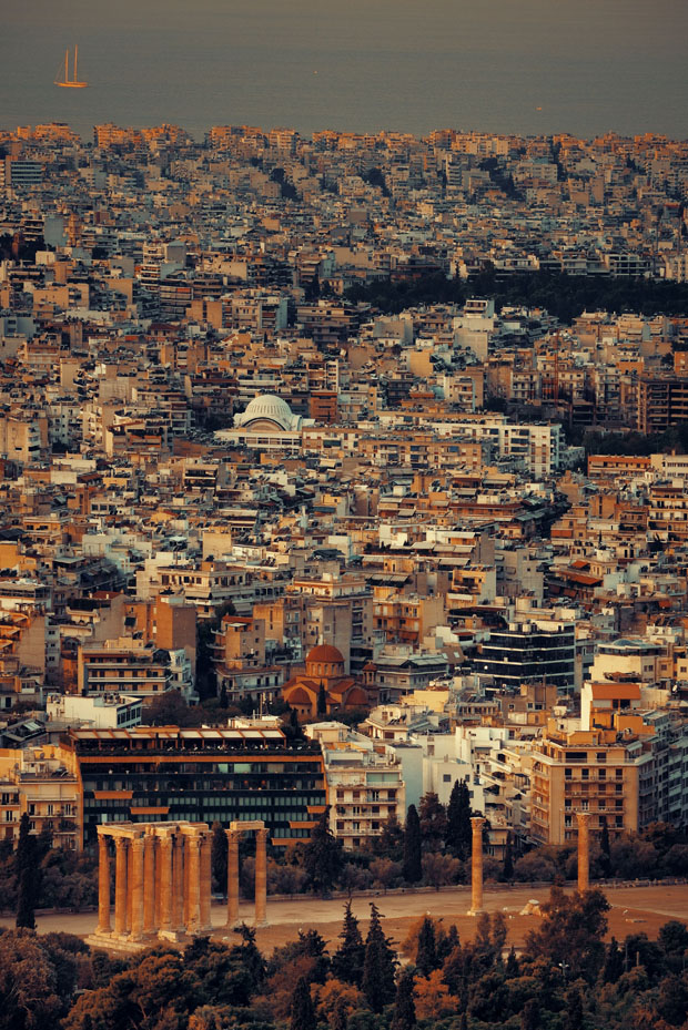 Sky view over Athens Greece with the Saronic Gulf in the distance, with orange tinted lights from sunset coming on