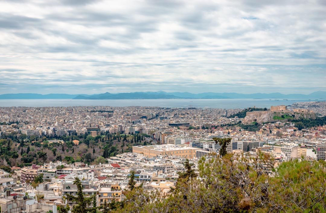 View of the Saronic Bay in the distance, with Syntagma the seat of parliament and the former Royal palace of the Kings of Greece in the view at the middle with the city of Athens spread out to the waters edge - Salamis island in view