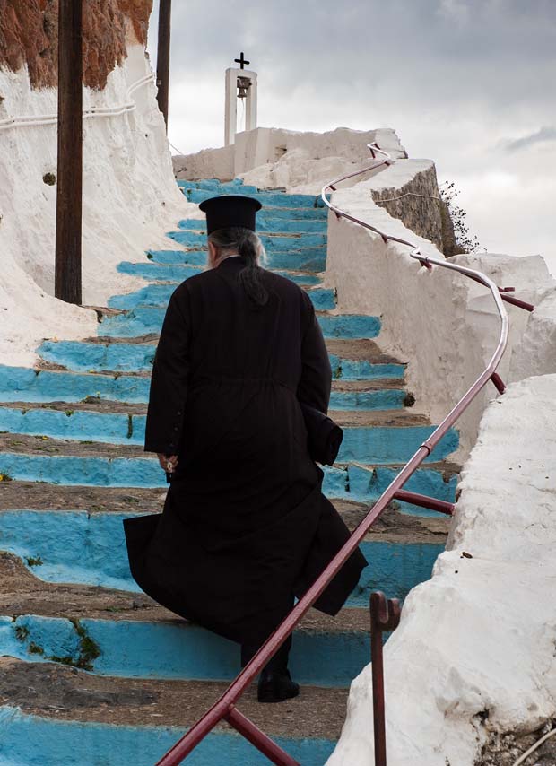 A black robed priest walking up white washed steps in the Peloponnese